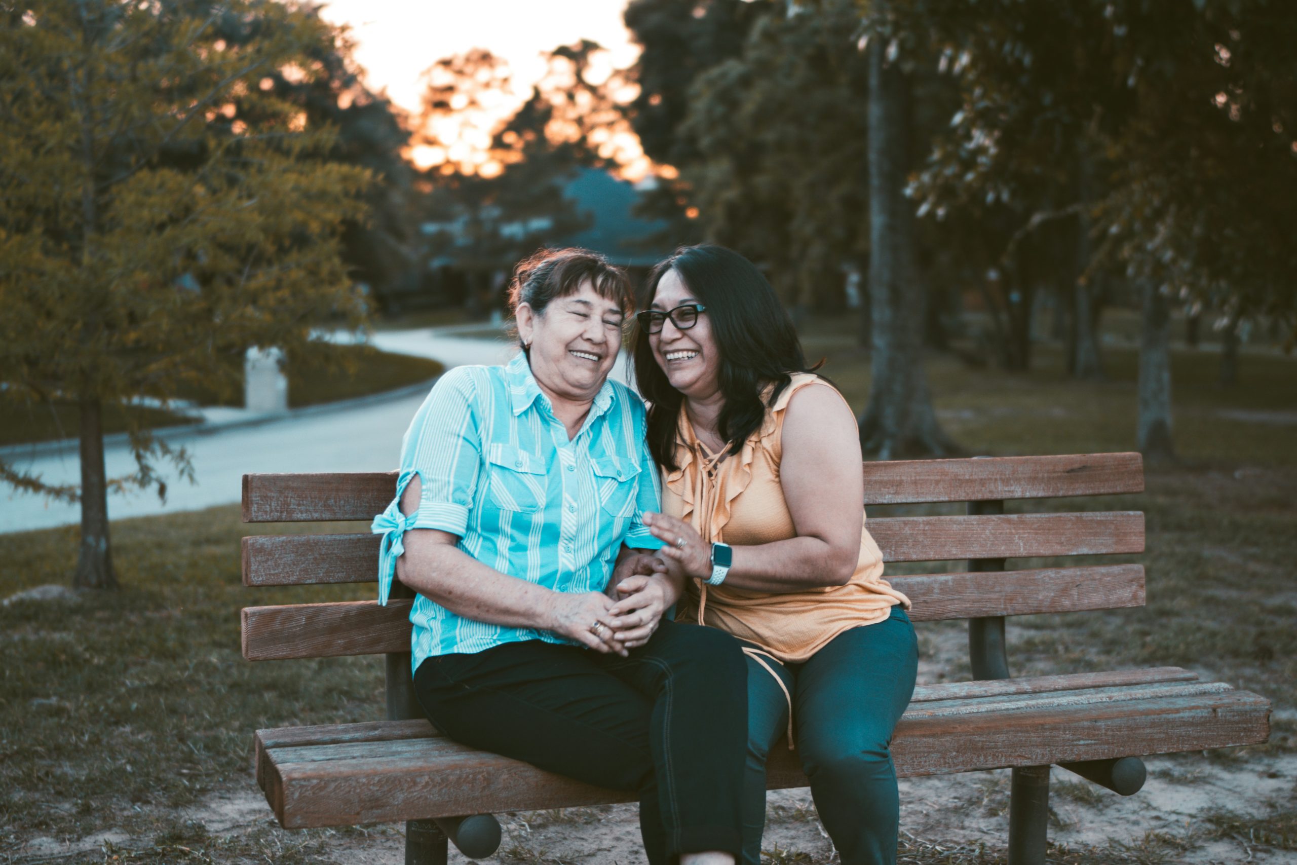 A mother and daughter hug sit affectionately on a park bench.