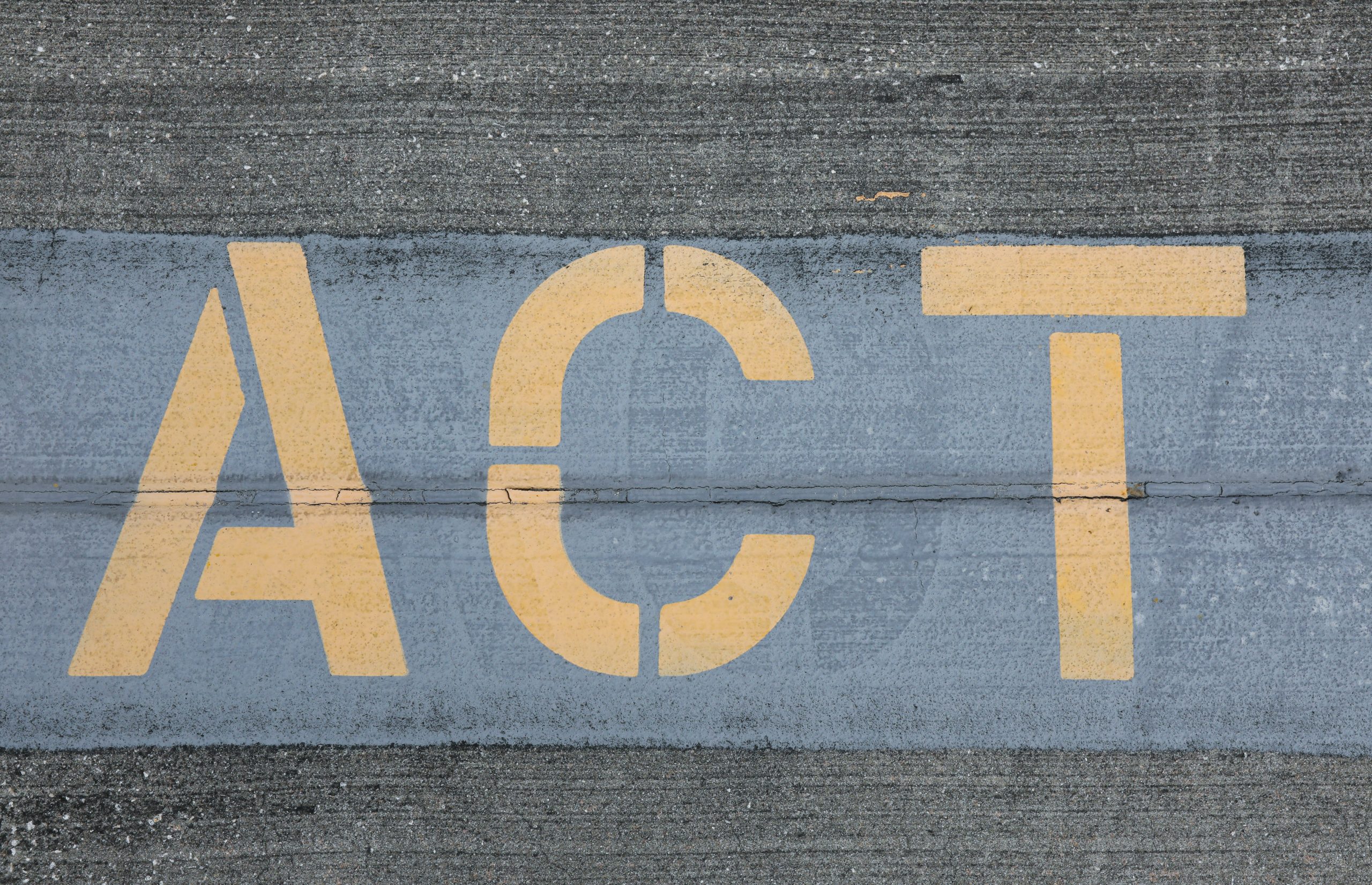 Large stenciled and spray painted letters say "ACT" on a concrete road