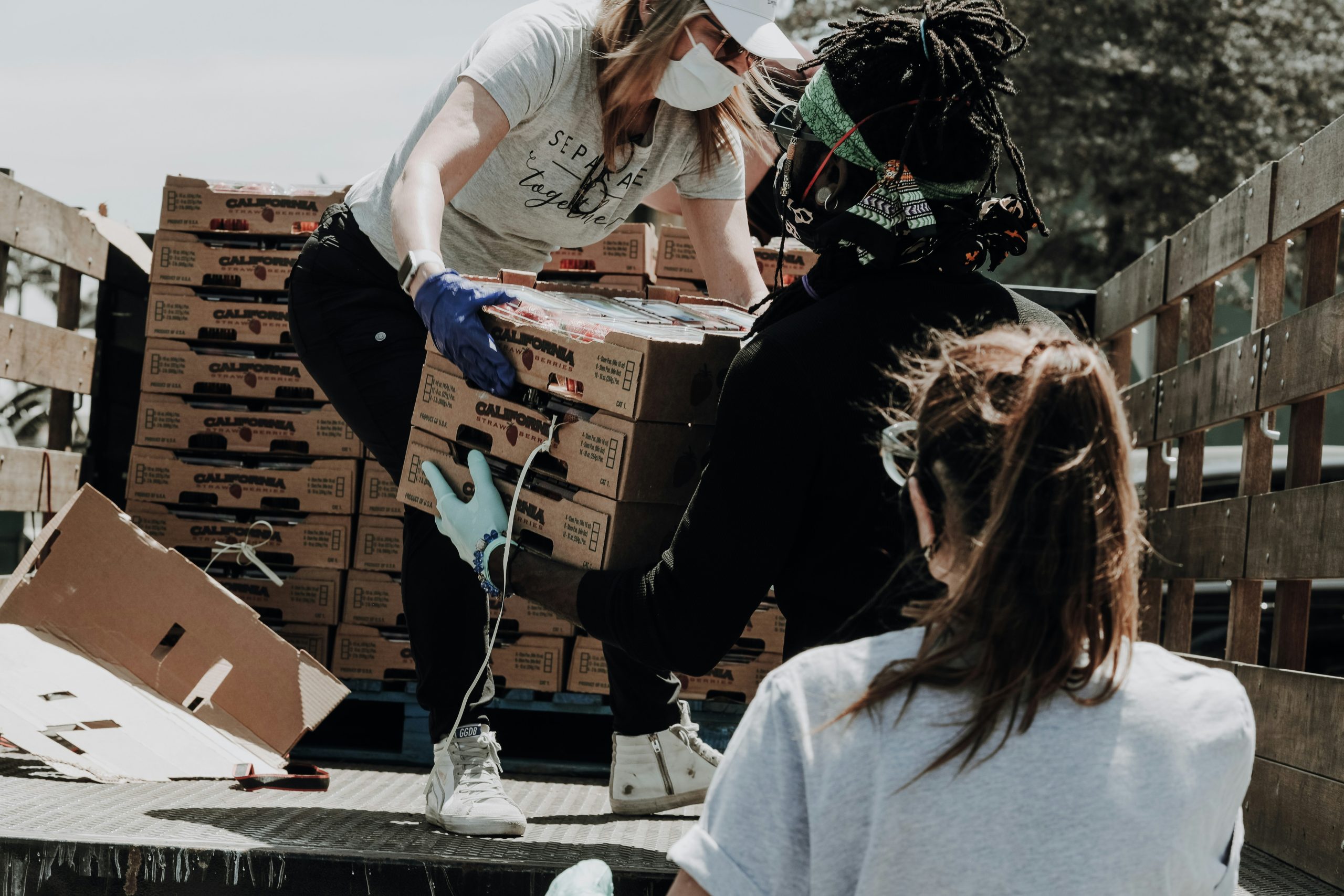 One volunteer passes a box of food to another from the bed of a truck
